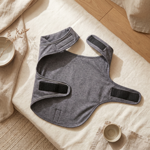 Gray calming dog vest with adjustable straps on cozy linen, ideal for pet anxiety relief and comfort.