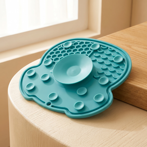 Teal slow feeder mat for cats and dogs with puzzle textures and central bowl, placed on wooden surface near window