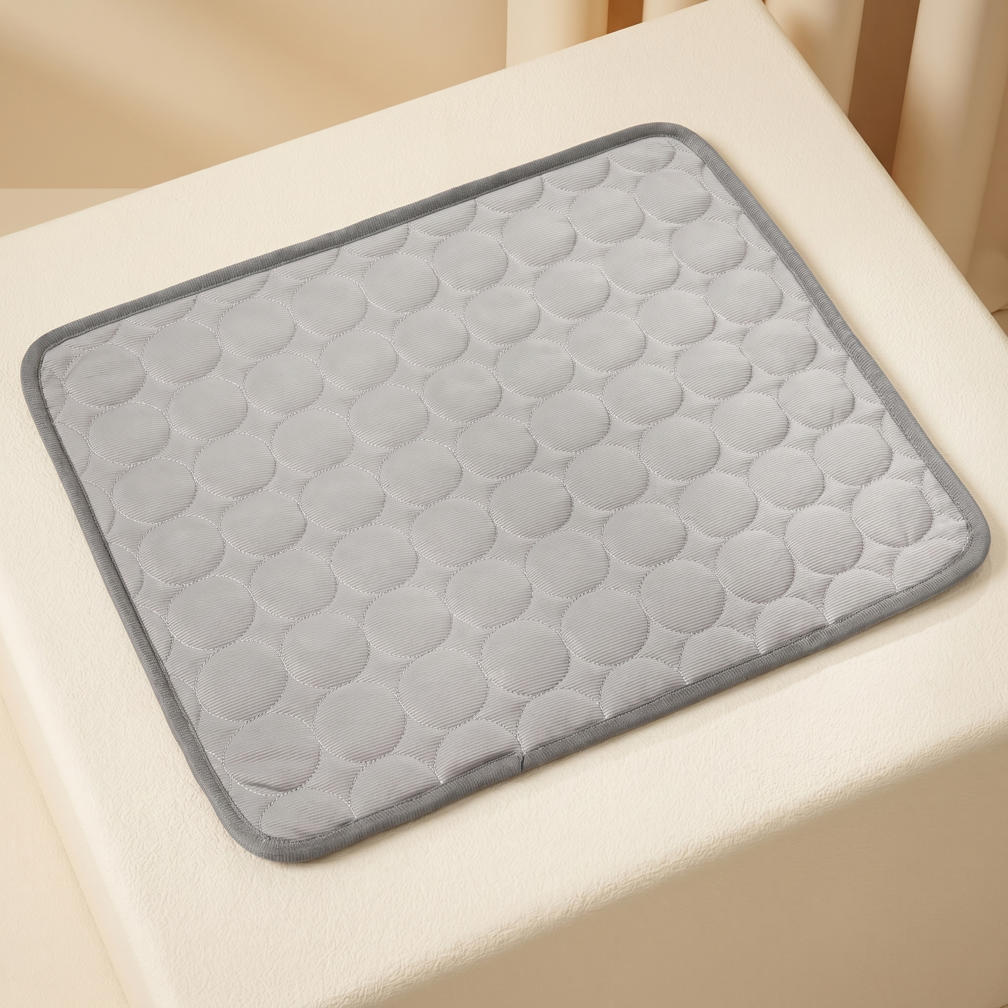 Gray quilted cooling mat for cats and dogs, featuring circular pattern, placed on cream pet bed for comfort.